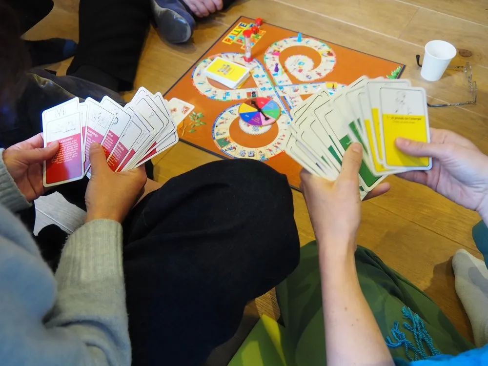Mains tenant des cartes du jeu au-dessus d’un plateau posé au sol