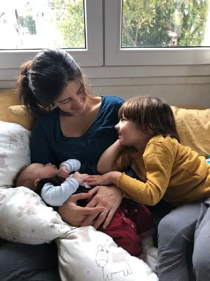 Une mère allaite son nourrisson, son jeune enfant blotti contre elle sur le canapé.