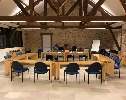 Salle de l’école aménagée pour un atelier-conférence : tables en U et chaises sous une charpente en bois