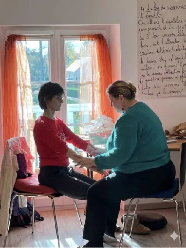 Une praticienne tient les mains d’une personne assise face à elle pendant une séance.