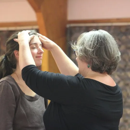 Une praticienne pose les mains sur le front d’une personne, pendant une séance